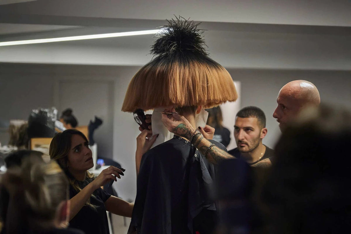 Backstage di una sfilata: hair stylist al lavoro su un taglio a fungo arancione