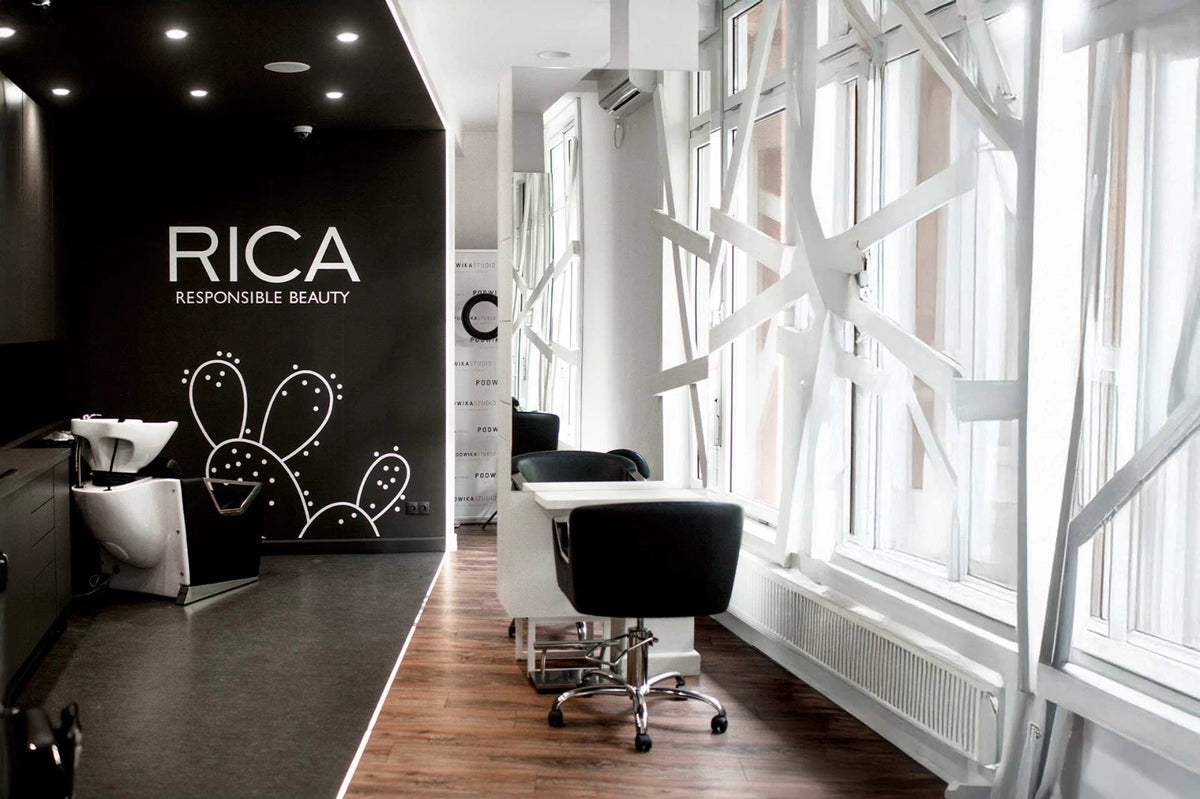 Salone Rica: parete nera con il logo RICA Responsible Beauty e un disegno di fico d'India bianco, poltrona nera e vetrate